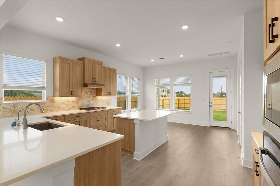Kitchen featuring decorative backsplash, light wood-style floors, a kitchen island, light countertops, and recessed lighting