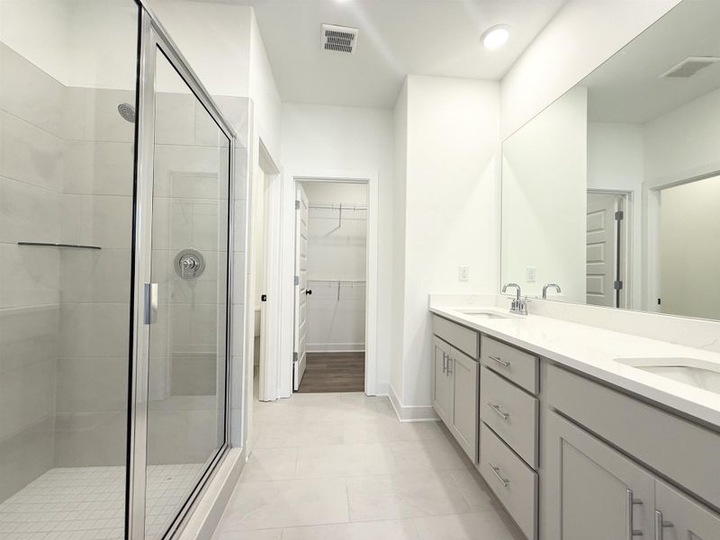 Bathroom with double vanity, a shower stall, a walk in closet, and light tile patterned floors