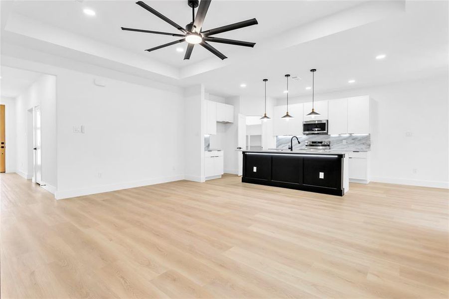 Unfurnished living room with light wood-type flooring, a tray ceiling, ceiling fan, and recessed lighting