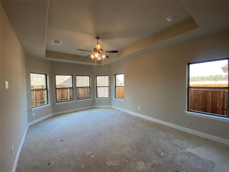 Master bedroom offers tray ceiling, bay window seating area, and ceiling a fan.