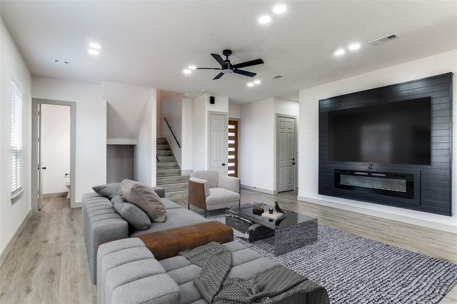 Living area featuring stairs, light wood-style floors, a ceiling fan, a large fireplace, and recessed lighting Living area featuring stairs, light wood-style floors, a ceiling fan, a large fireplace, and recessed lighting