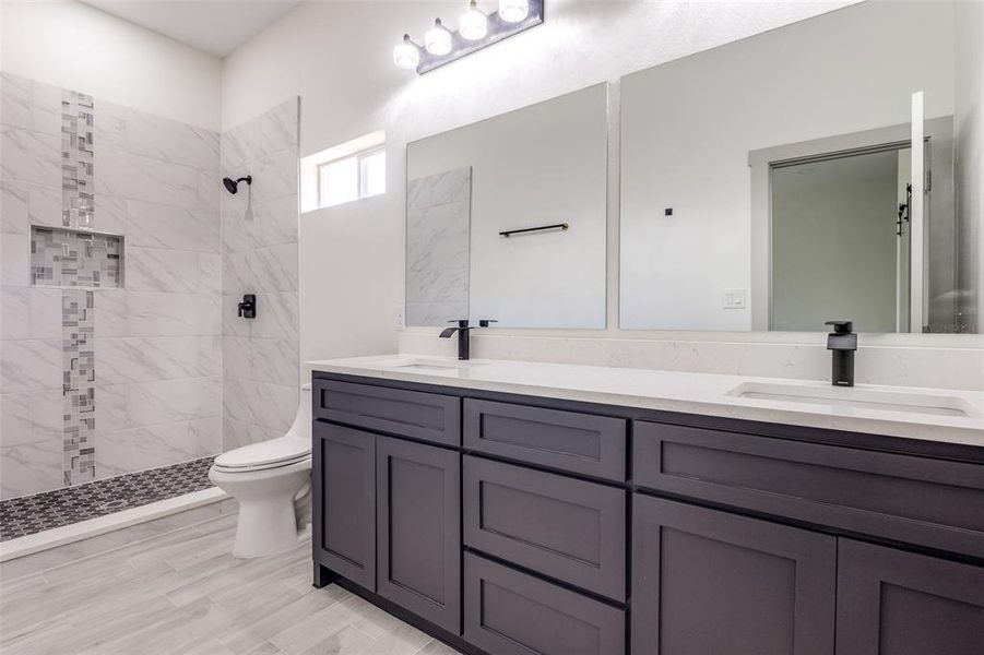 Bathroom with a tile shower, vanity, and toilet