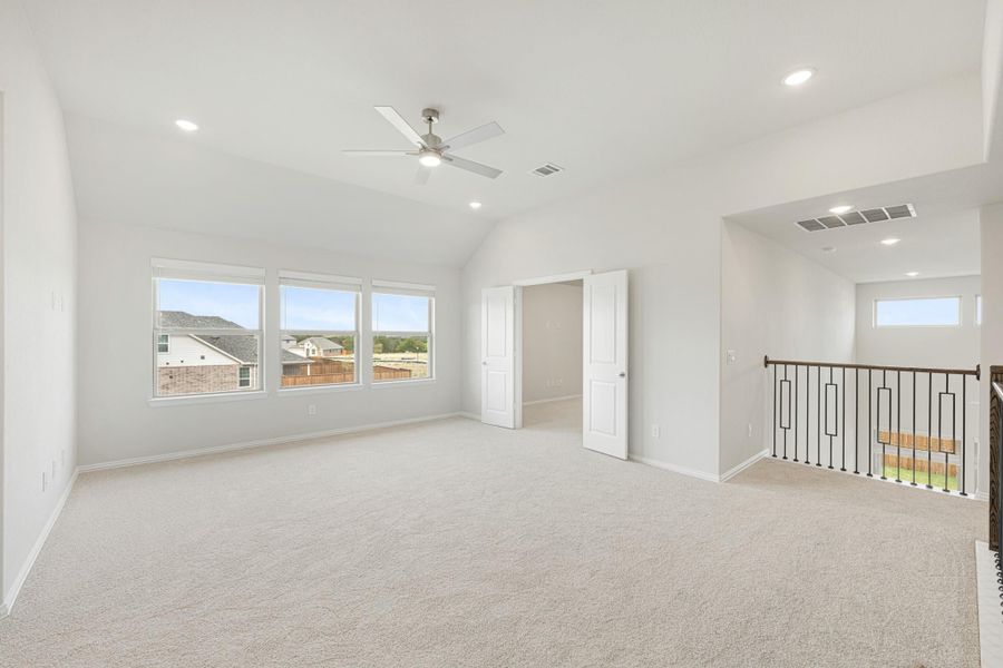 Spacious upstairs bonus room with vaulted ceiling, ceiling fan, carpet, and open staircase railing