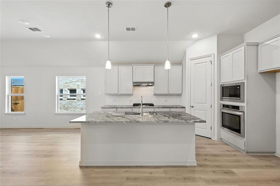 Kitchen featuring stainless steel appliances, light stone countertops, decorative backsplash, white cabinets, and an island with sink Kitchen featuring stainless steel appliances, light stone countertops, decorative backsplash, white cabinets, and an island with sink