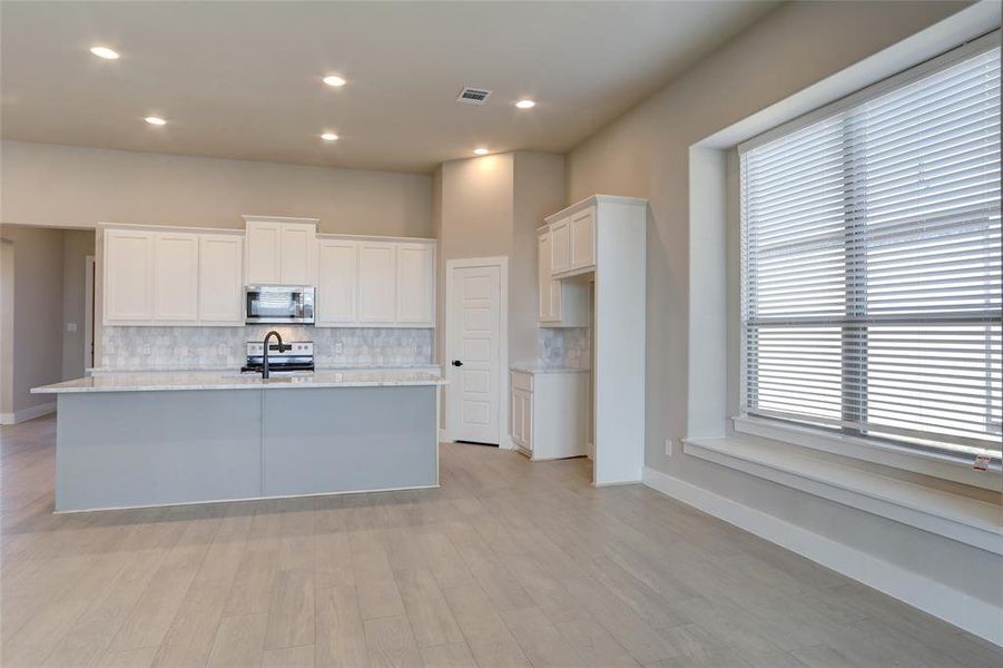 Kitchen featuring light hardwood / wood-style flooring, white cabinetry, a kitchen island with sink, stainless steel appliances, and tasteful backsplash