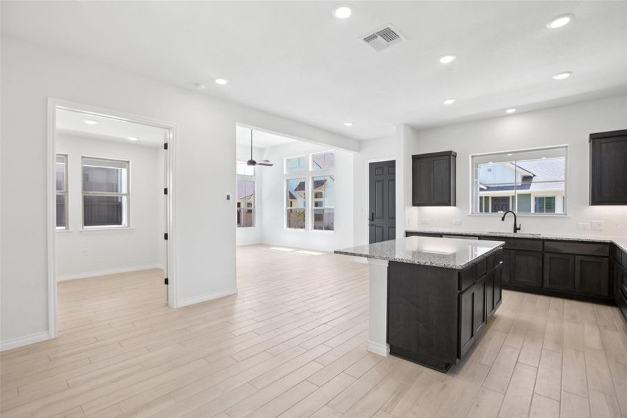 Kitchen with a kitchen island, light stone countertops, recessed lighting, open floor plan, and light wood-type flooring