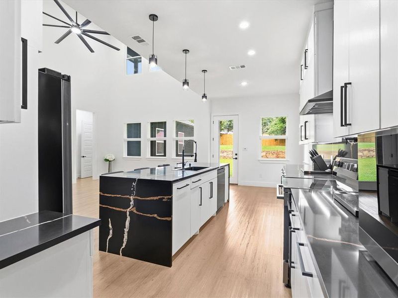 Modern kitchen featuring an expansive island with a waterfall edge and striking veining, white cabinetry, dark countertops, and stainless steel appliances