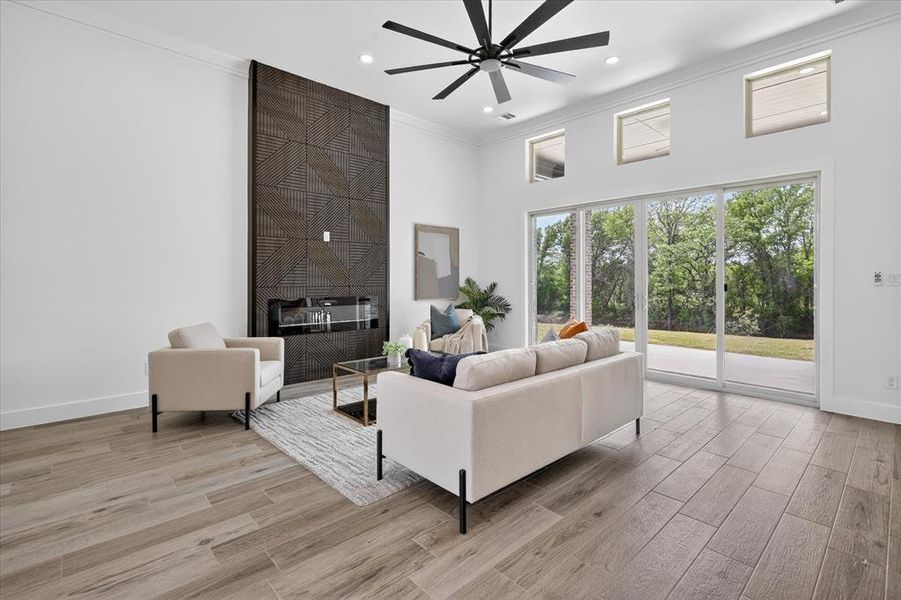 Living room with a high ceiling, wood finish floors, a fireplace, ceiling fan, and ornamental molding