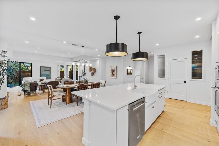 Kitchen featuring white cabinetry, hanging light fixtures, an island with sink, light wood-type flooring, and recessed lighting