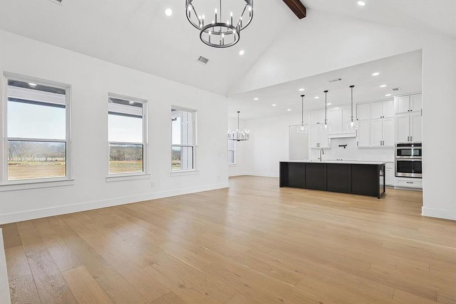 Unfurnished living room with beamed ceiling, sink, an inviting chandelier, and light hardwood / wood-style flooring