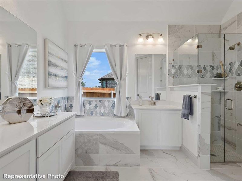 Bathroom featuring a built-in tub, a walk-in shower with a glass enclosure, dual vanities with white cabinetry, and patterned tile accents