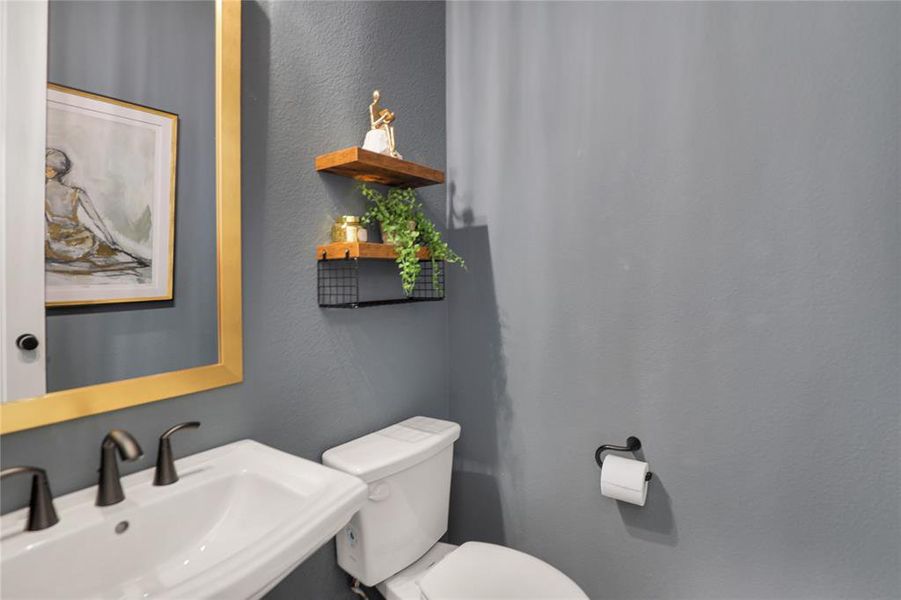 Pedestal sink with dark bronze faucet, framed mirror, and two-tier wall shelving
