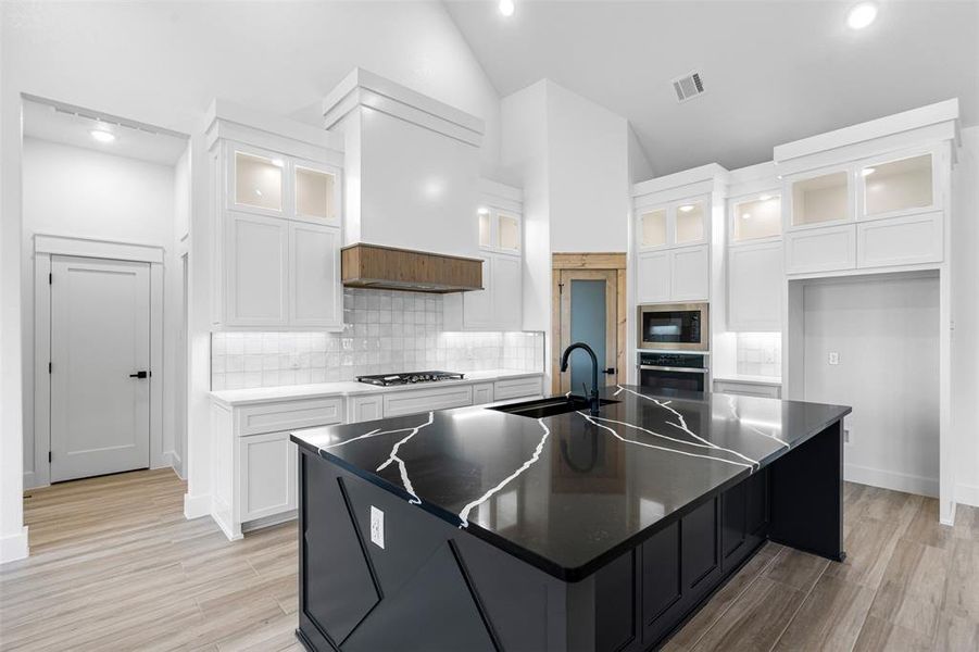 Kitchen featuring a spacious island, backsplash, white cabinetry, appliances with stainless steel finishes, and sink