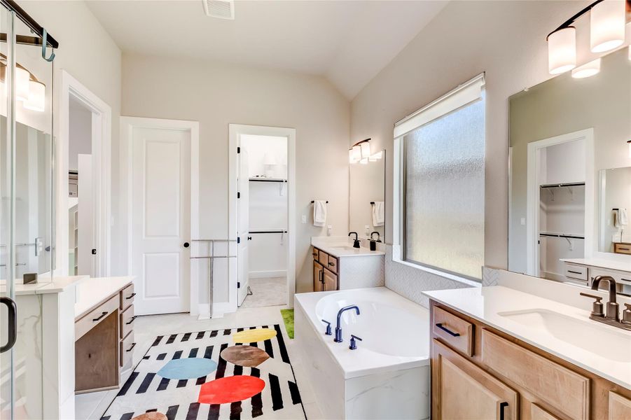 A well-lit bathroom features a deep soaking tub and dual vanities, complemented by bright white finishes.