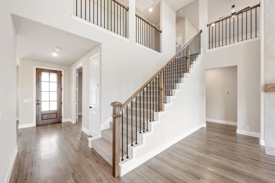 Two-story foyer with wood staircase, metal balusters, hardwood floors, and glass-panel front door