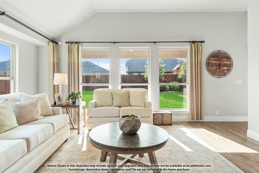 Living room with vaulted ceiling, hardwood floors, large windows, and cream sofas around a round coffee table Living room with vaulted ceiling, hardwood floors, large windows, and cream sofas around a round coffee table