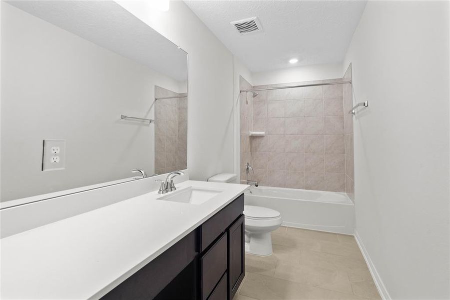 Secondary bath features tile flooring, bath/shower combo with tile surround, stained wood cabinets, beautiful light countertops, mirror, sleek and modern finishes.