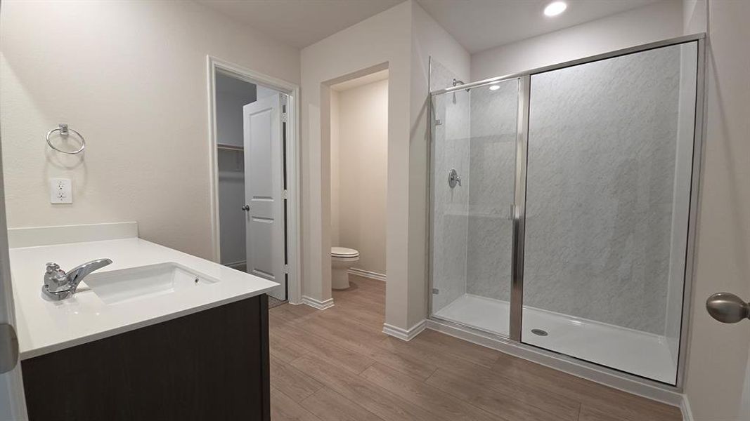 Spacious bathroom with wood-finish flooring, a contemporary vanity featuring a white countertop and integrated sink, and a glass-enclosed shower with subway tile surround Spacious bathroom with wood-finish flooring, a contemporary vanity featuring a white countertop and integrated sink, and a glass-enclosed shower with subway tile surround