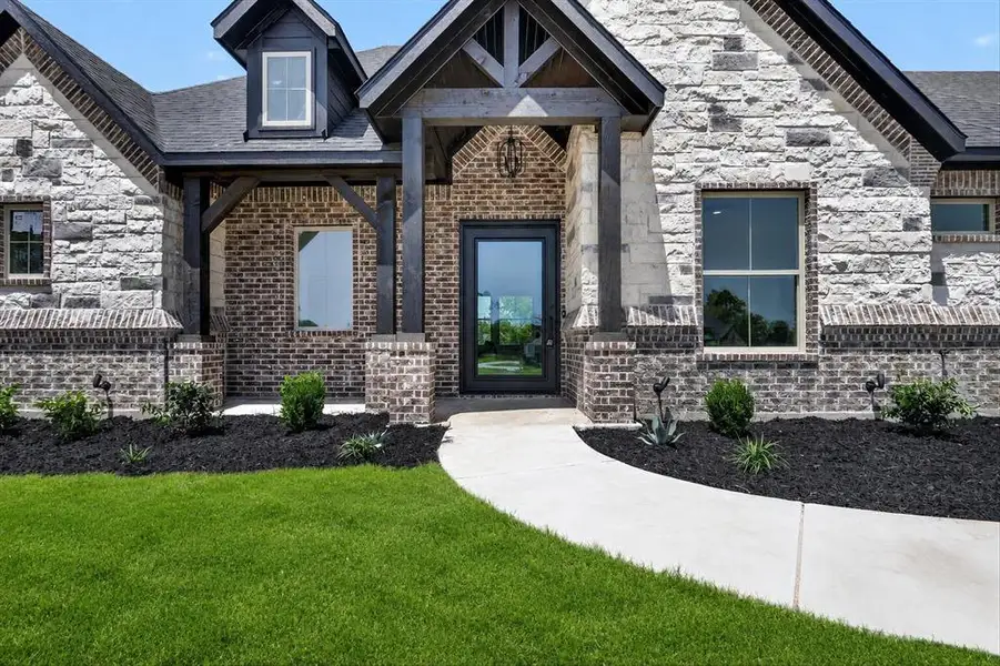 Crafted exterior featuring a glass-panel entry door, dark brick, and light stone accents