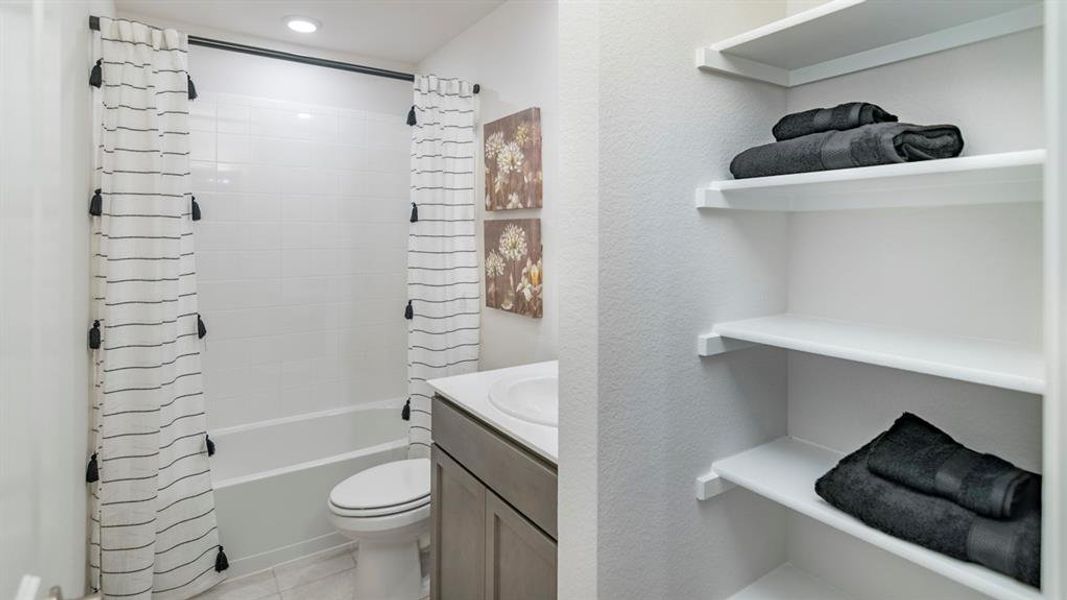 Bathroom featuring vanity, shower / bath combination with curtain, light tile patterned floors, and a textured wall Bathroom featuring vanity, shower / bath combination with curtain, light tile patterned floors, and a textured wall