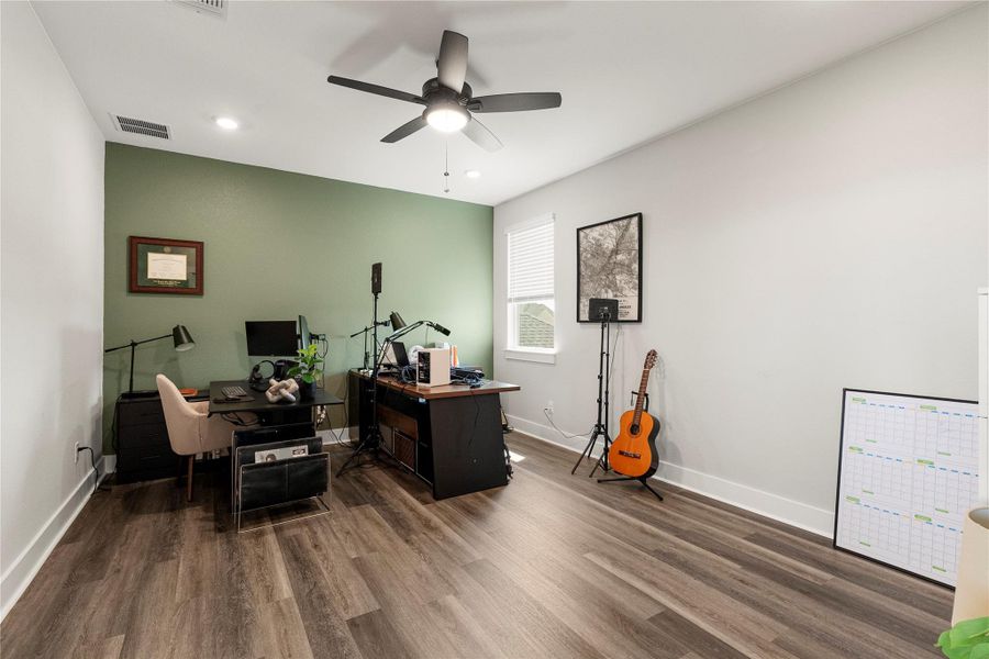 An airy office space features wood flooring and a refreshing accent wall. An airy office space features wood flooring and a refreshing accent wall.