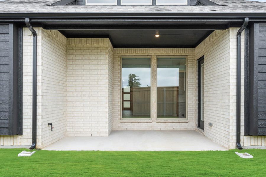 Covered back patio with white brick walls, dark trim, sliding glass door, and concrete floor overlooking green lawn