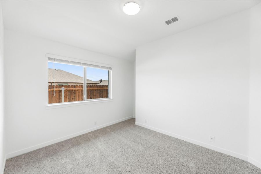 Empty bedroom with white walls, gray carpet, and a single window with backyard view