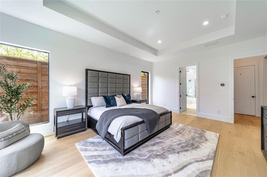 Bedroom featuring a tray ceiling, recessed lighting, light wood-type flooring, and ensuite bathroom