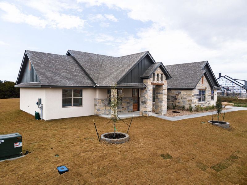 View of front facade with roof with shingles, stone siding, board and batten siding, and a front lawn