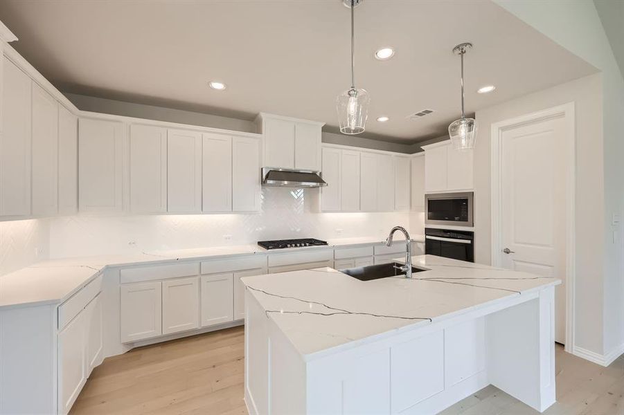 Kitchen featuring a center island with sink, stainless steel oven, white cabinetry, light hardwood / wood-style flooring, and sink