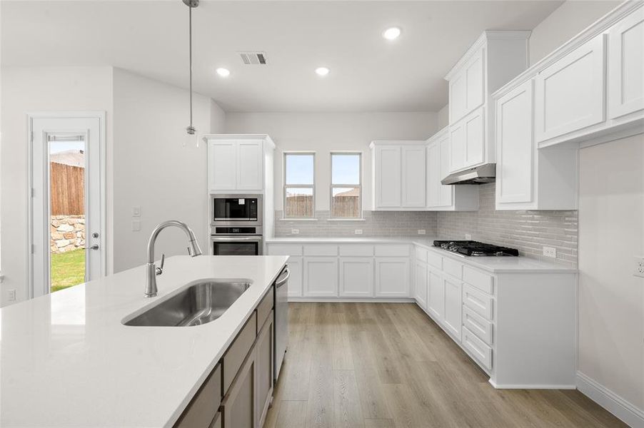 Kitchen featuring stainless steel appliances, under cabinet range hood, light wood finished floors, decorative backsplash, and recessed lighting