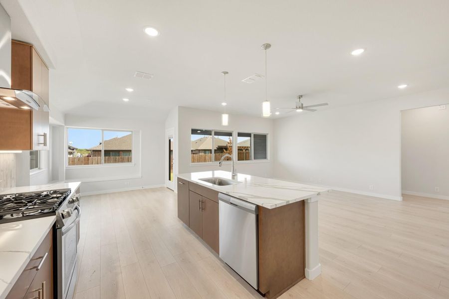 Open kitchen with center island, quartz countertops, stainless appliances, and light wood floors opening to living area