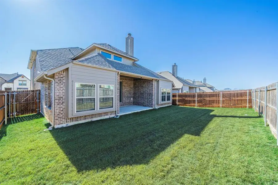 Expansive rear lawn featuring a covered patio, brick and siding exterior, multiple windows, and a full perimeter fence