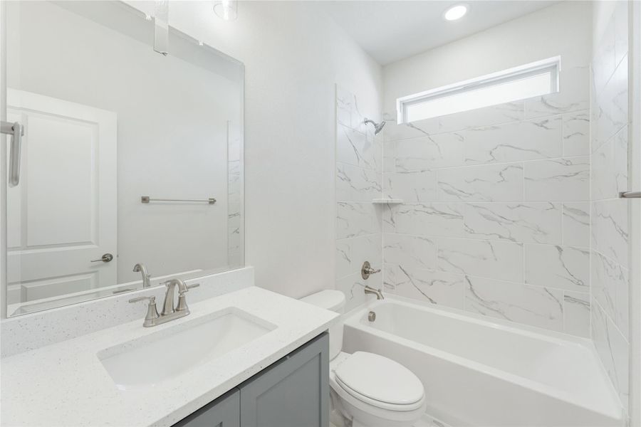 Bathroom with gray vanity, quartz countertop, and tub-shower combo with marble-look tile surround