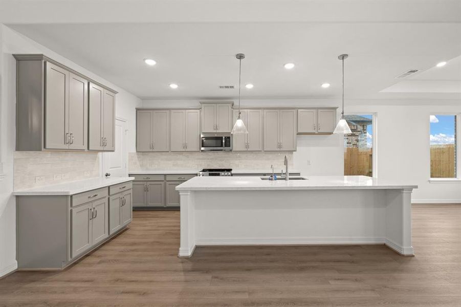 This light and bright kitchen features a large quartz island, white cabinets, a large sink overlooking your family room, recessed lighting, and beautiful backsplash.