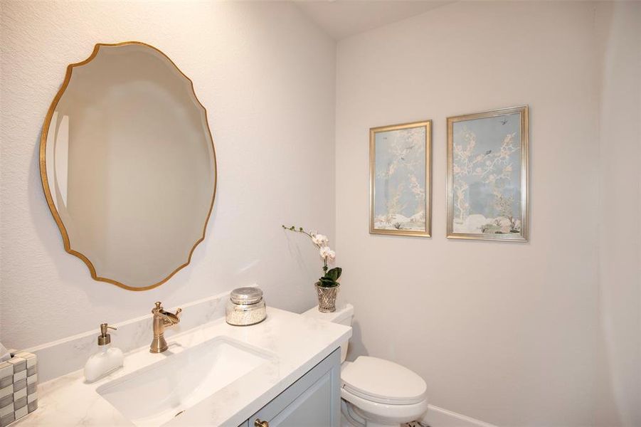 This photo showcases a modern, elegant bathroom with a stylish vanity featuring a marble countertop, ornate mirror, and gold fixtures. Two framed artworks add a touch of sophistication.