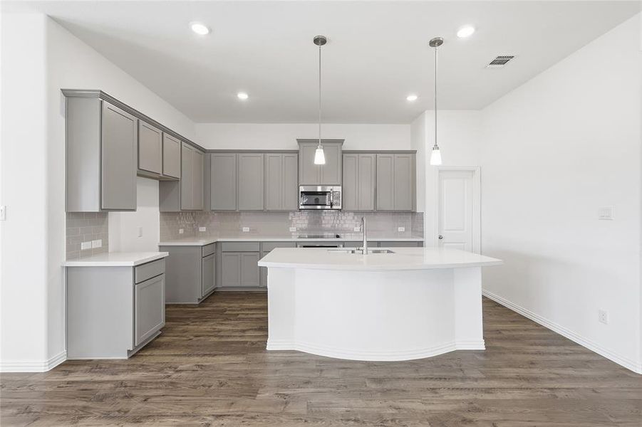 Modern kitchen featuring a large central island, light gray cabinetry, stainless steel appliances, a tile backsplash, and wood-finish flooring