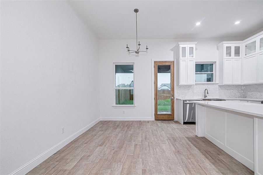 Kitchen featuring a chandelier, light countertops, light wood-style flooring, tasteful backsplash, and white cabinetry Kitchen featuring a chandelier, light countertops, light wood-style flooring, tasteful backsplash, and white cabinetry