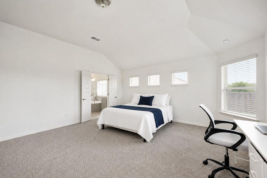 A well-lit bedroom with vaulted ceilings and plush carpeting, offering a private retreat connected to an en-suite bathroom.