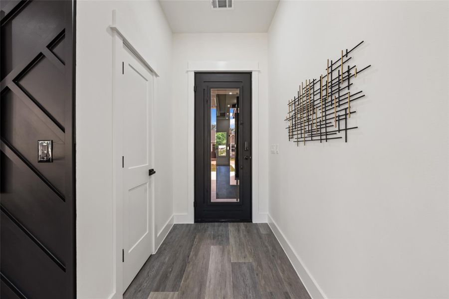Entryway featuring wood-finish flooring, a full-lite door with dark trim, white interior doors, and a decorative wall panel with geometric patterns