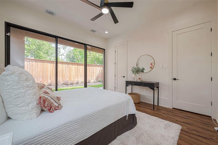 This is a bright and modern bedroom featuring large windows with a view of the backyard, sleek hardwood floors, and contemporary decor. A ceiling fan provides comfort, and the room is spacious with a minimalist feel. This is a bright and modern bedroom featuring large windows with a view of the backyard, sleek hardwood floors, and contemporary decor. A ceiling fan provides comfort, and the room is spacious with a minimalist feel.