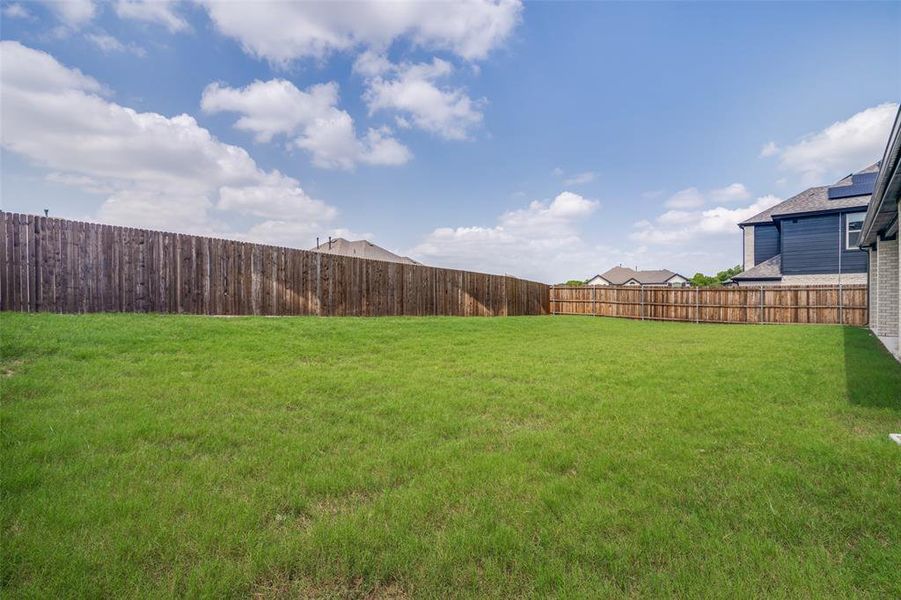 Expansive backyard featuring a lush green lawn, full wood privacy fencing, and a light brick and dark siding exterior on the property