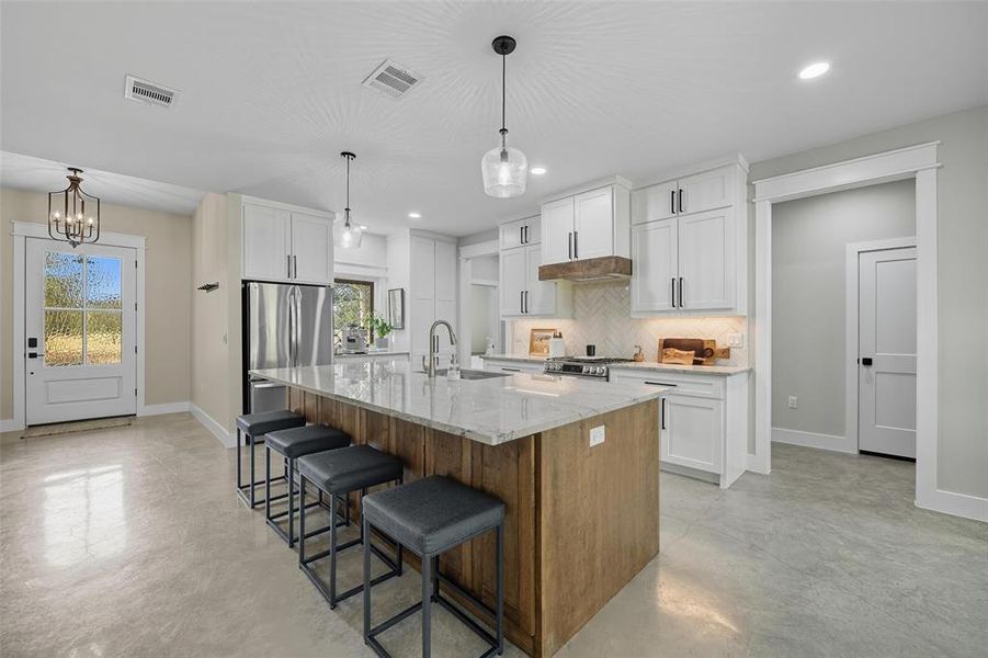 Kitchen featuring brown cabinetry, an island with sink, tasteful backsplash, white cabinets, and recessed lighting Kitchen featuring brown cabinetry, an island with sink, tasteful backsplash, white cabinets, and recessed lighting