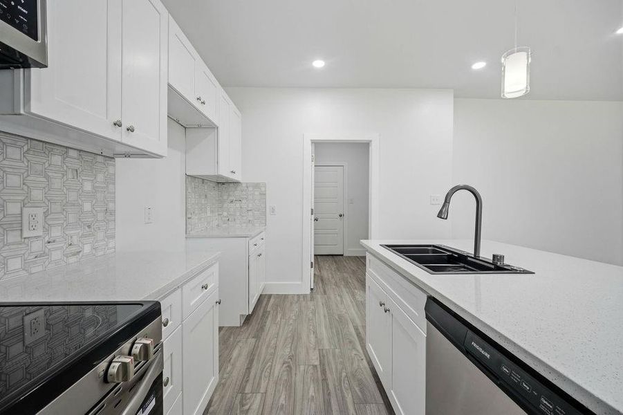 Modern kitchen featuring white shaker cabinetry, light-toned countertops, a geometric pattern tile backsplash, a stainless steel electric range, and a kitchen island with an undermount sink and stainless steel dishwasher Modern kitchen featuring white shaker cabinetry, light-toned countertops, a geometric pattern tile backsplash, a stainless steel electric range, and a kitchen island with an undermount sink and stainless steel dishwasher