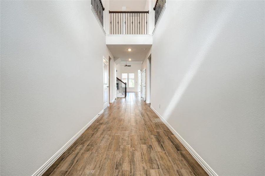Hall featuring wood finished floors, a towering ceiling, and stairs Hall featuring wood finished floors, a towering ceiling, and stairs