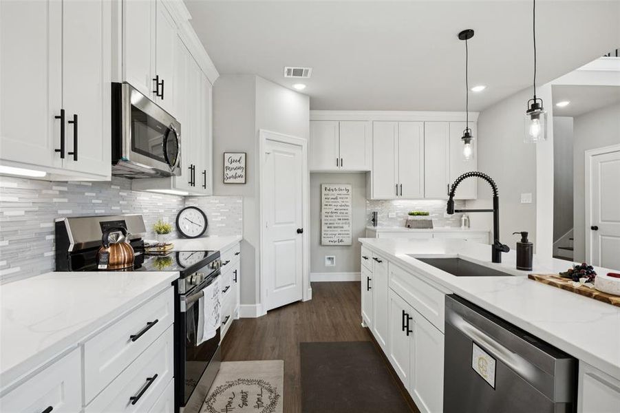 Kitchen with appliances with stainless steel finishes, white cabinetry, tasteful backsplash, decorative light fixtures, and light stone counters