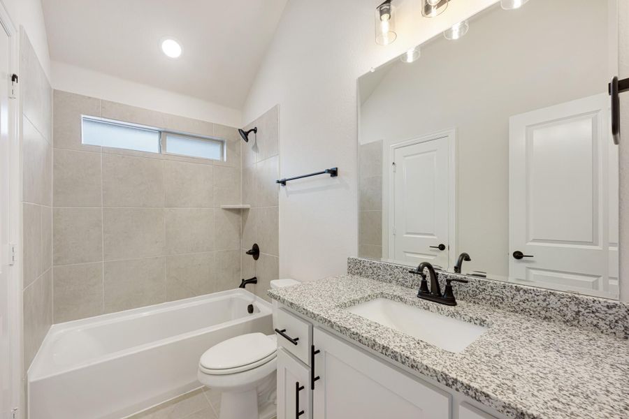 Bathroom with granite countertop vanity, tiled tub-shower combo, and vaulted ceiling with black fixtures Bathroom with granite countertop vanity, tiled tub-shower combo, and vaulted ceiling with black fixtures