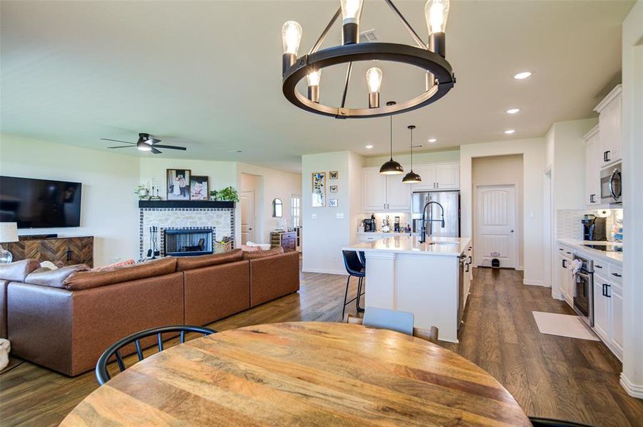 Dining room with dark wood-type flooring, a fireplace, a ceiling fan, and hanging lights