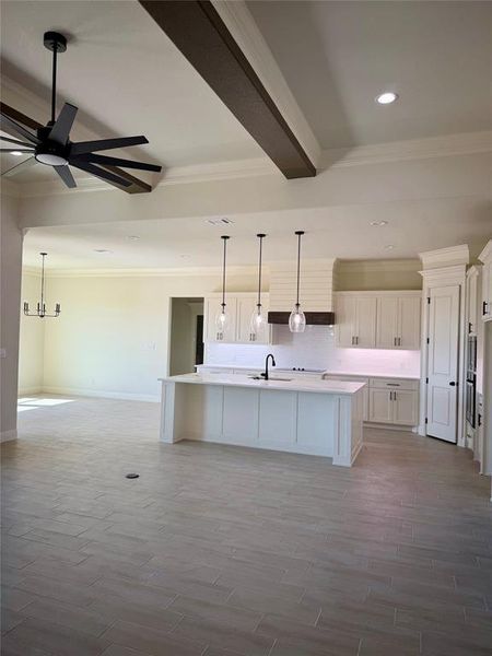 Kitchen with an island with sink, hanging light fixtures, white cabinets, ornamental molding, and open floor plan Kitchen with an island with sink, hanging light fixtures, white cabinets, ornamental molding, and open floor plan