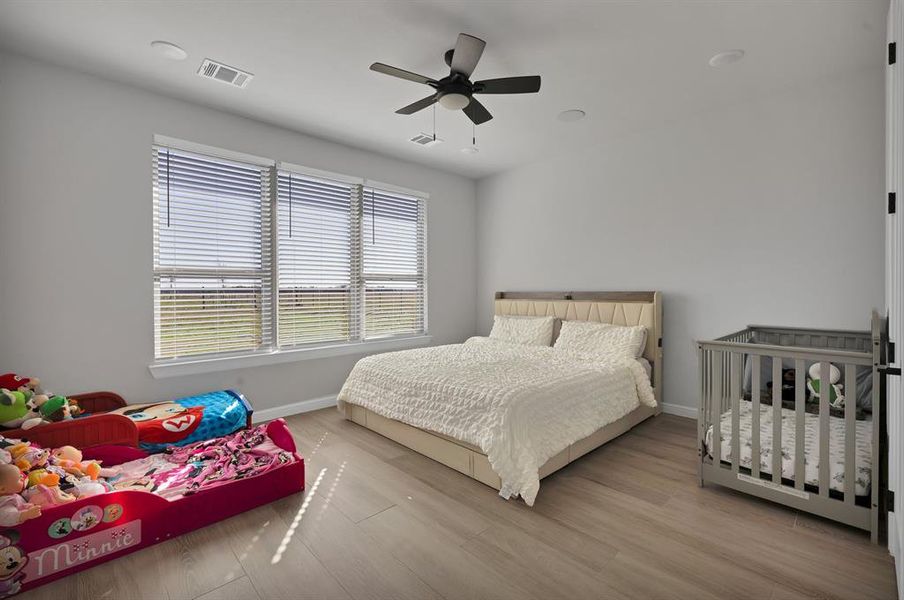 Bedroom with ceiling fan, wood finished floors, visible vents, and baseboards